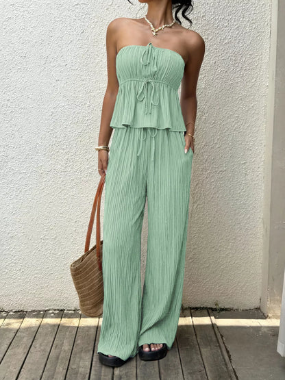 Woman wearing light green wide leg trouser pants for women with a matching strapless top and carrying a woven bag