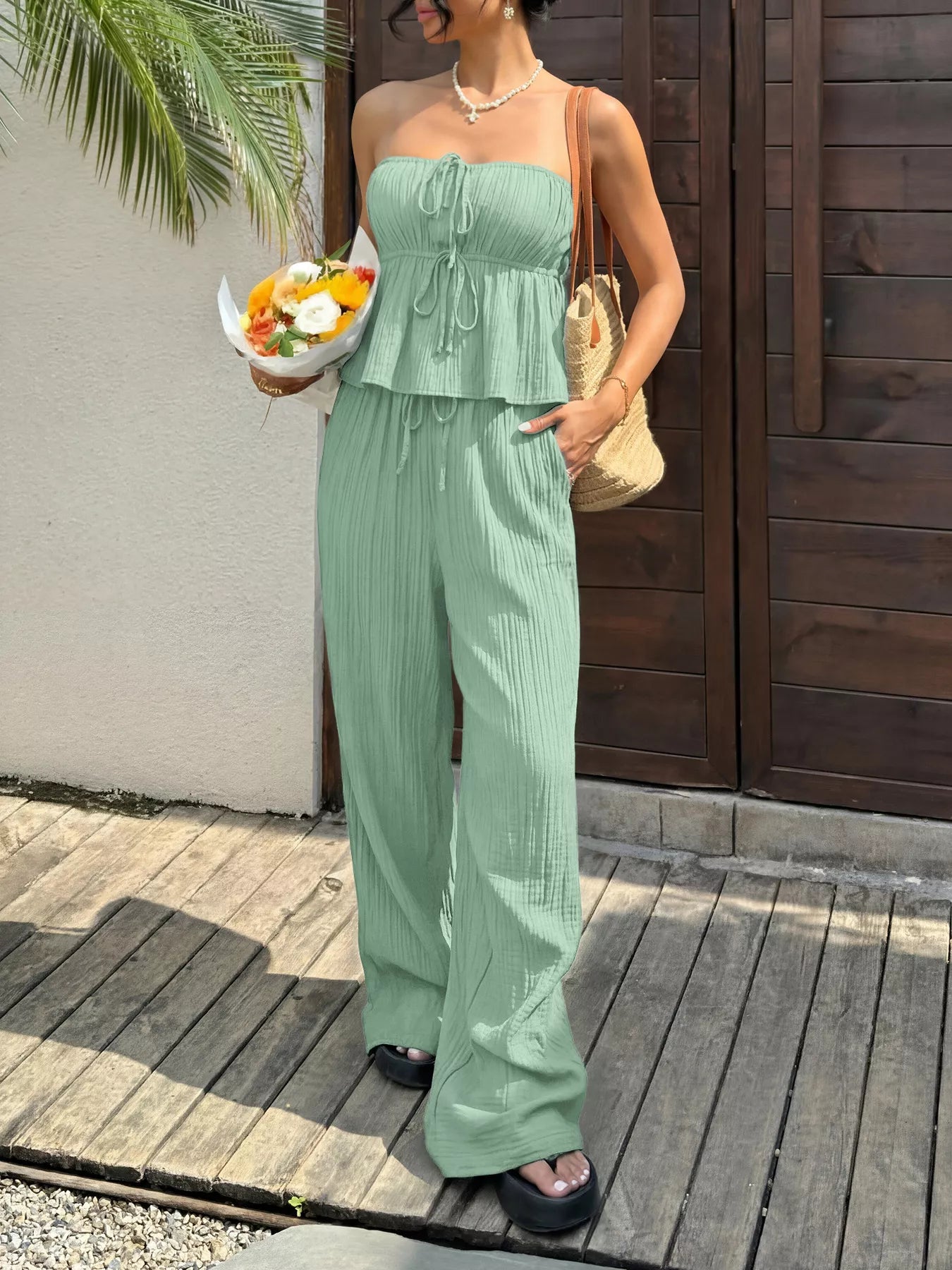 Woman wearing green wide leg trouser pants for women with matching strapless top holding flowers