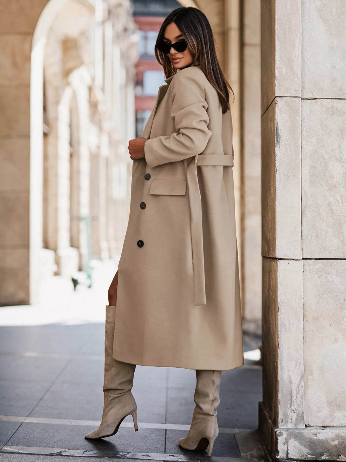 Woman wearing beige double breasted coat trench with belt and black buttons paired with knee-high boots
