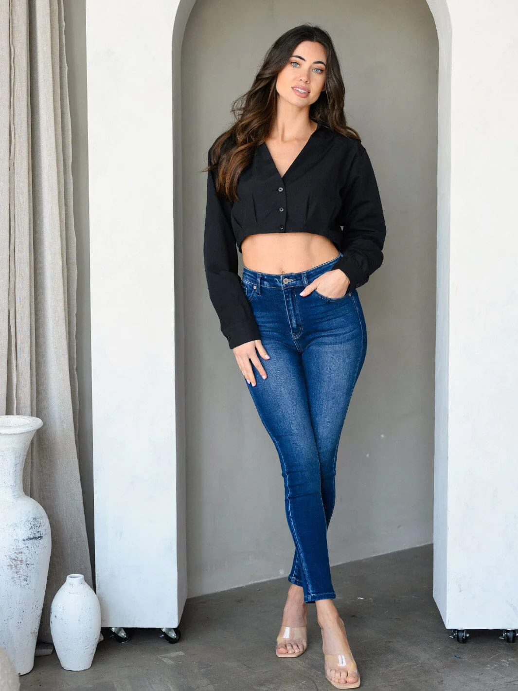 Woman wearing women's black crop top long sleeve button-up paired with blue skinny jeans and clear heels